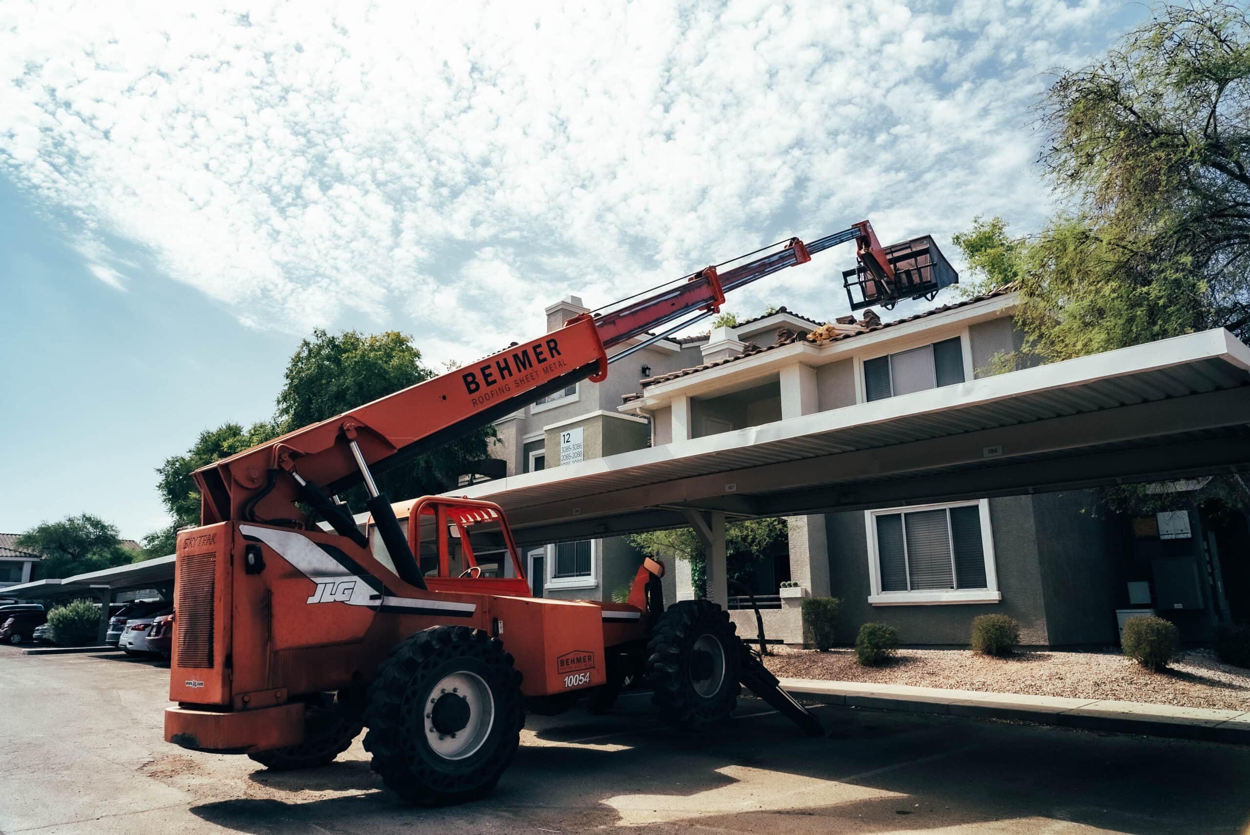 A crane lifts an ironwood roof in front of an apartment building.