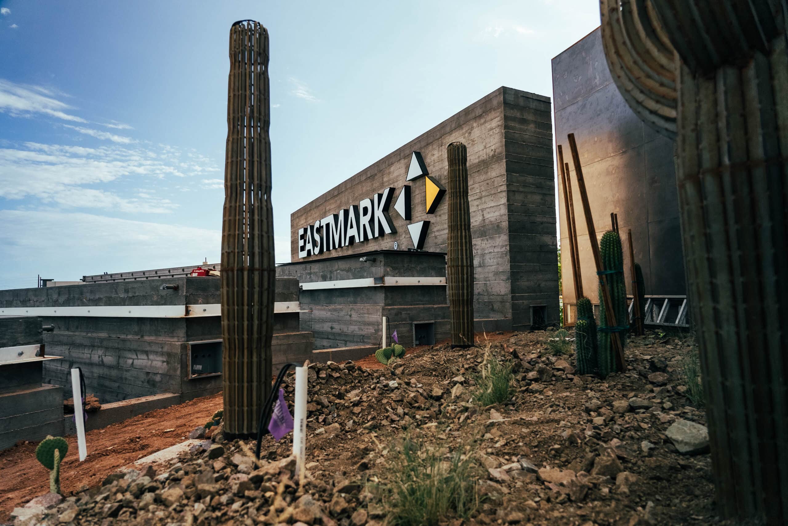A north Phoenix roofing contractor stands beside a cactus in front of their building with a sign.