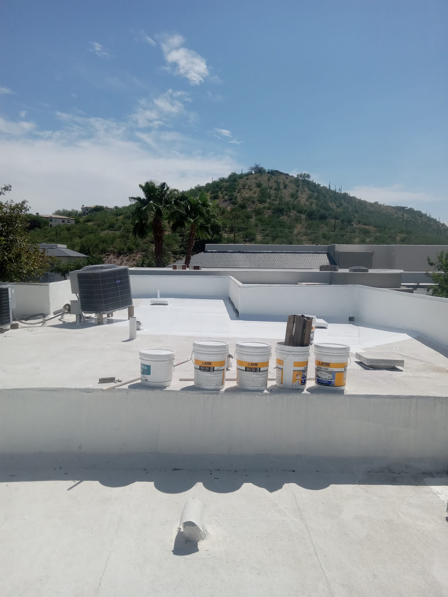 A white roof coated with Chandler's innovative solution and equipped with white buckets, all against the picturesque backdrop of a mountain.
