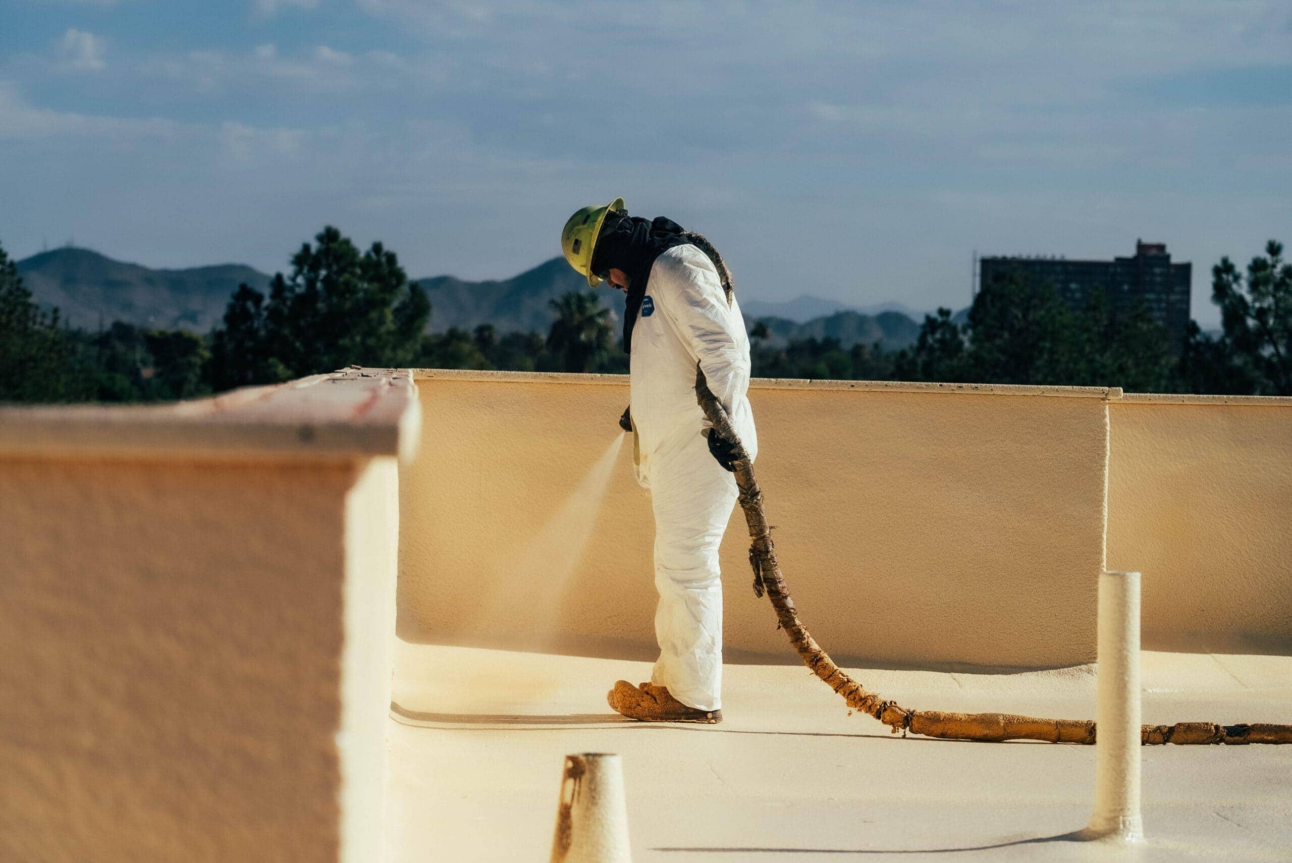 A professional in protective gear applies coating over spray foam on a rooftop in the serene Whisper Rock area.