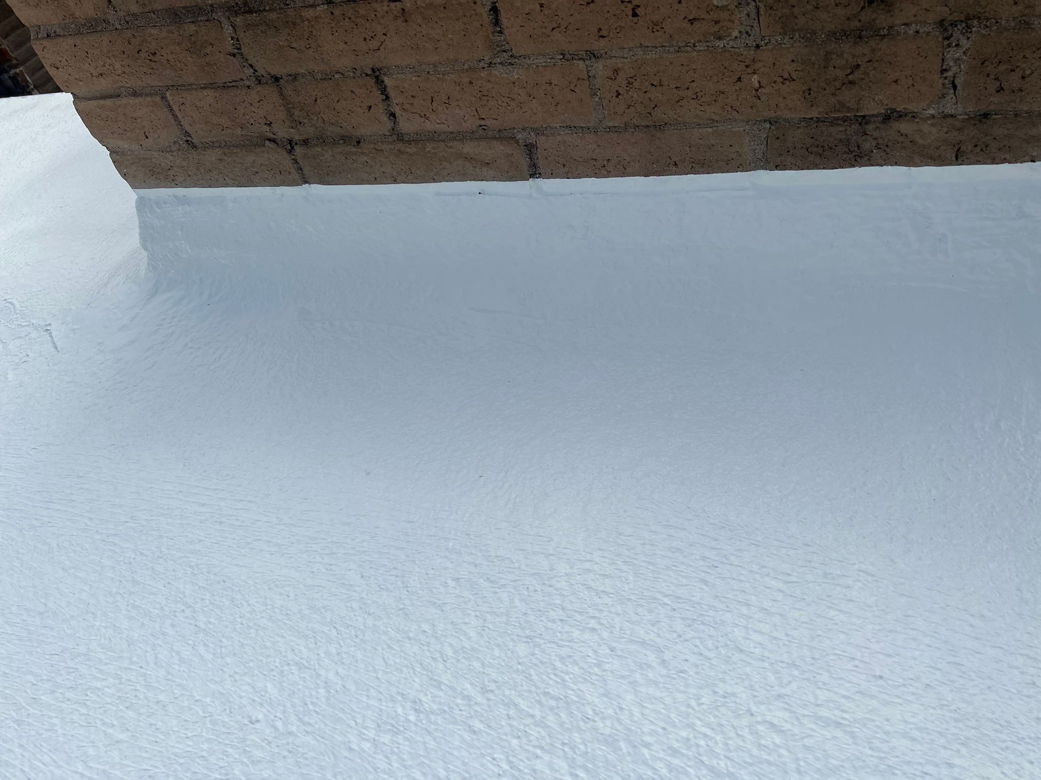 Detailed shot of a foam roof beside a brick wall in a Peoria home, showing the neat application.