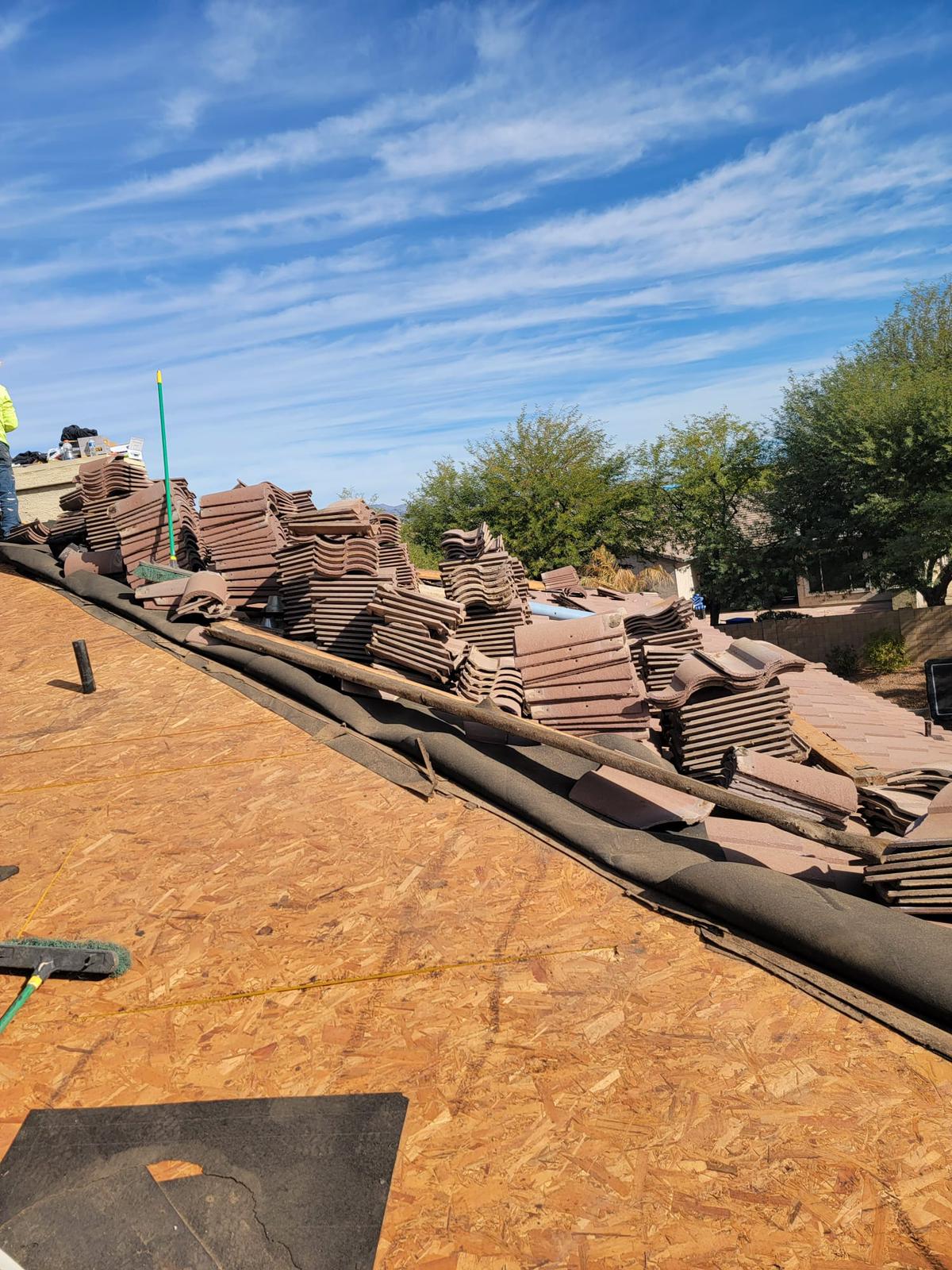 Overview of a Phoenix home mid-renovation, featuring piles of neatly stacked tiles ready for a Behmer re-felt service, against a backdrop of a clear blue sky.