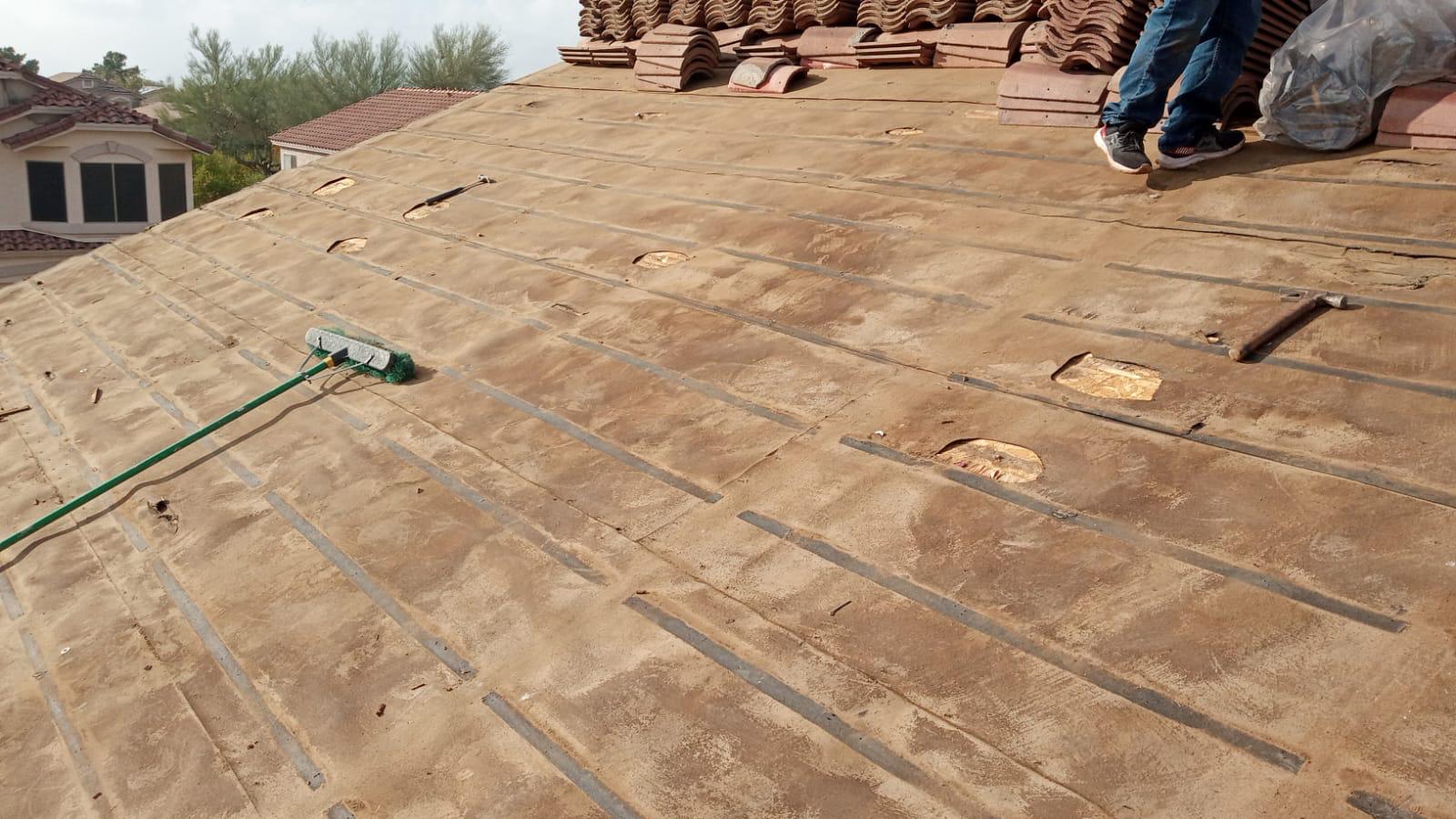A man is working on the roof of a house in Grayhawk, re-felting the tiles.